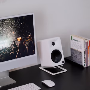 Bàn đen tối giản với iMac, loa bookshelf trắng trên chân đế, bàn phím Magic, chuột và sách Branding 4.0