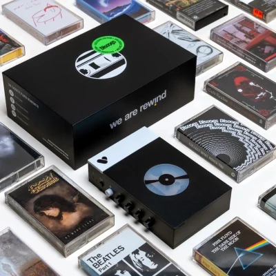 Ảnh flat lay: máy cassette Discogs × We Are Rewind, hộp đen sticker Exclusive Edition Discogs xanh và nhiều băng cassette quanh viền