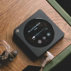 FiiO SnowSky DISC đen cùng tai IEM trong suốt trên mặt gỗ, màn hình phát bài Me and the Moon