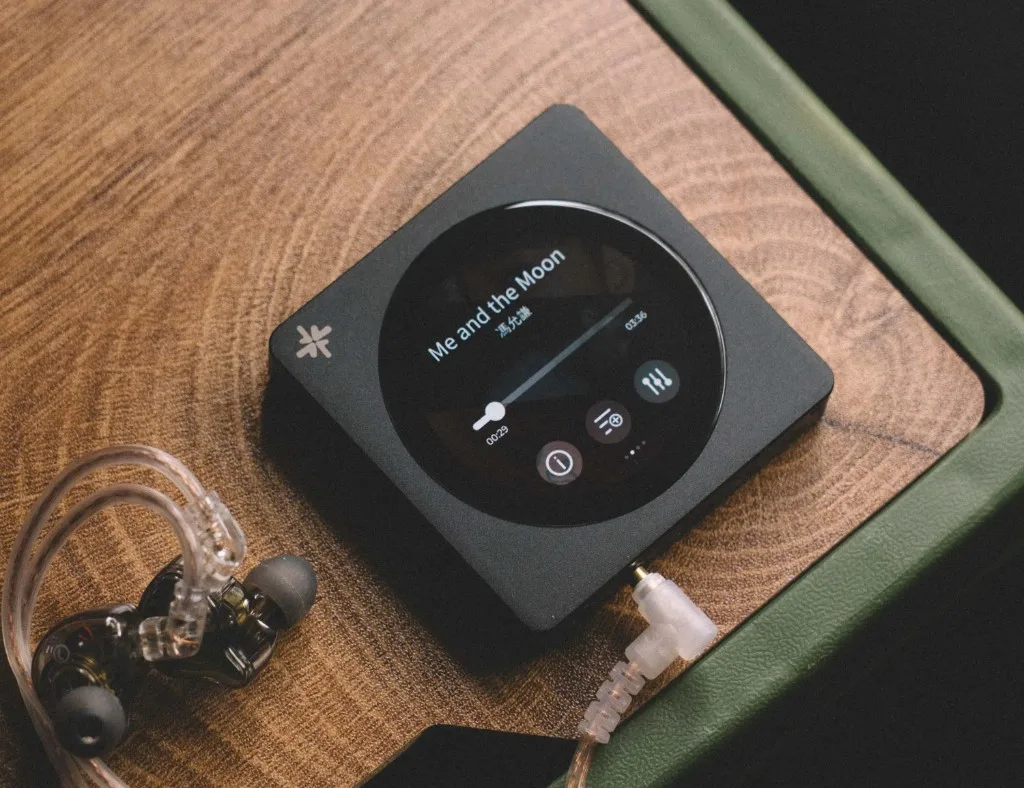 FiiO SnowSky DISC đen cùng tai IEM trong suốt trên mặt gỗ, màn hình phát bài Me and the Moon