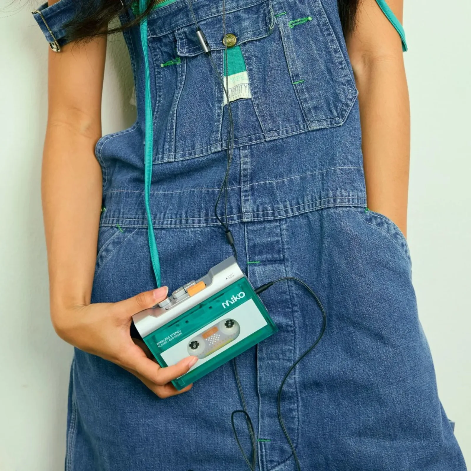 Gadhouse MIKO Mint cầm trên tay, yếm jean xanh, dây tai nghe, nền tường sáng