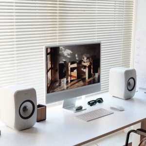 Hai loa KEF LSX II LT trắng hai bên iMac, bàn phím chuột Apple, kính râm, bàn trắng và rèm ngang