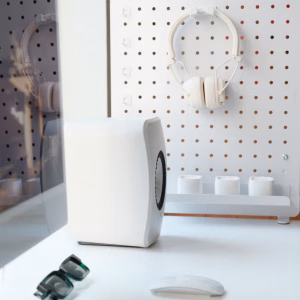 Loa bookshelf KEF LSX II LT trắng, pegboard, tai nghe trắng, kính râm và chuột trên bàn làm việc sáng