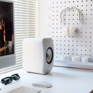 Loa KEF LSX II LT màu trắng trên bàn trắng, pegboard treo tai nghe, chuột Magic, kính râm và một phần iMac
