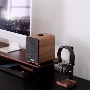 Loa Ruark gỗ cạnh tai nghe Marshall nâu trên giá đỡ kim loại đen đế gỗ, một phần iMac