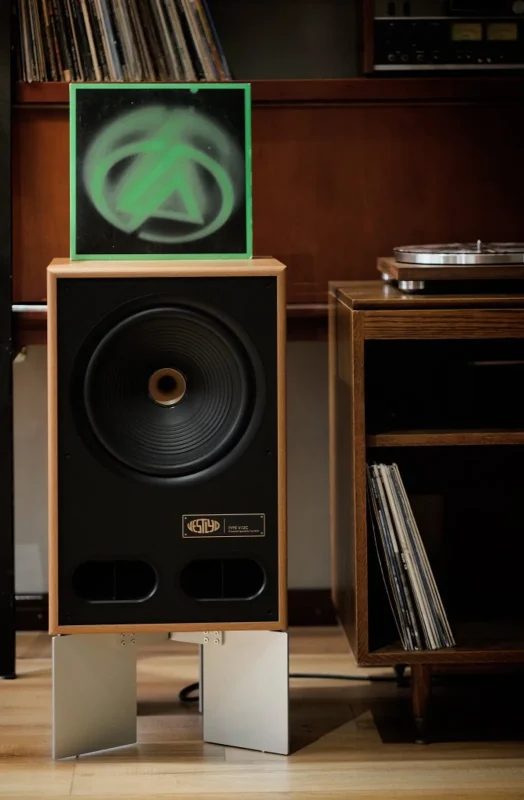 Loa cột Vestlyd V12C mặt trước đen, thùng gỗ sồi, driver đồng trục 12 inch và bảng tên đồng, đặt cạnh kệ và mâm than