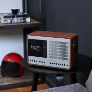 Radio Revo SuperConnect thùng gỗ Walnut mặt silver trên bàn đen, màn hình OLED hiển thị BBC Radio 6 Music trong phòng khách hiện đại.