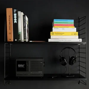 Revo SuperConnect phiên bản đen trên kệ sách kim loại cạnh tai nghe over-ear và sách thiết kế.