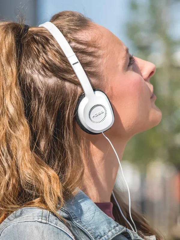 Người phụ nữ đeo tai nghe Koss KPH8 màu trắng on-ear ngoài trời, ánh sáng tự nhiên, tai nghe nhỏ gọn
