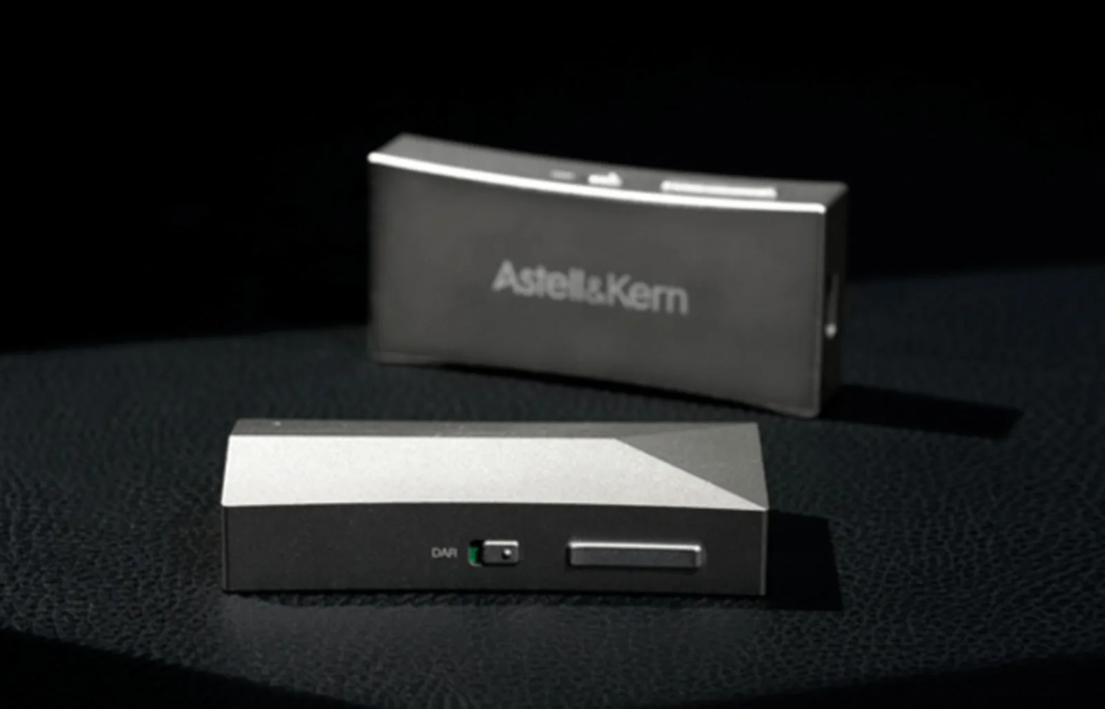 Hai AK HC4 bạc trên da đen: một máy thấy mặt logo Astell&Kern, một máy thấy mặt góc cạnh, công tắc DAR và nút volume dài.