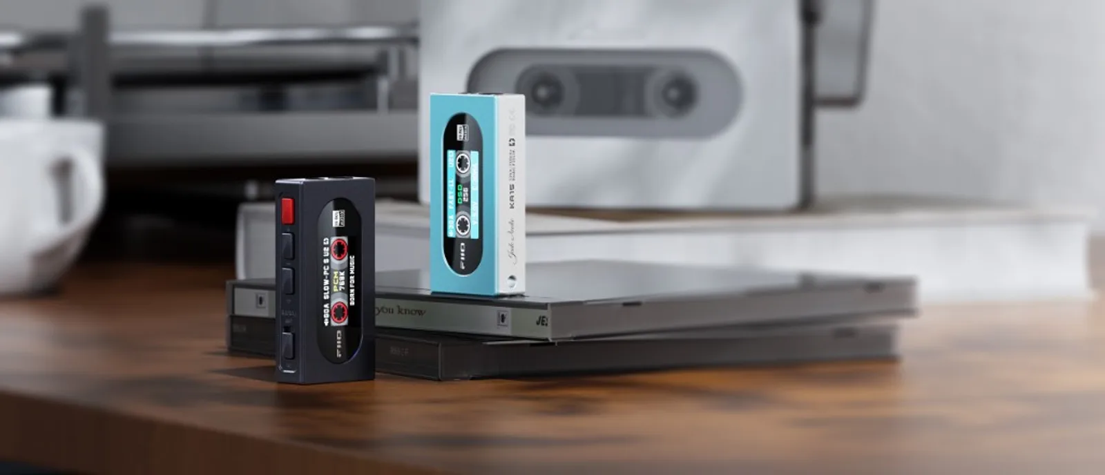 Hai FiiO KA15 màu đen và xanh đứng trên đĩa CD, màn hình hiển thị băng cassette và thông số DSD/PCM