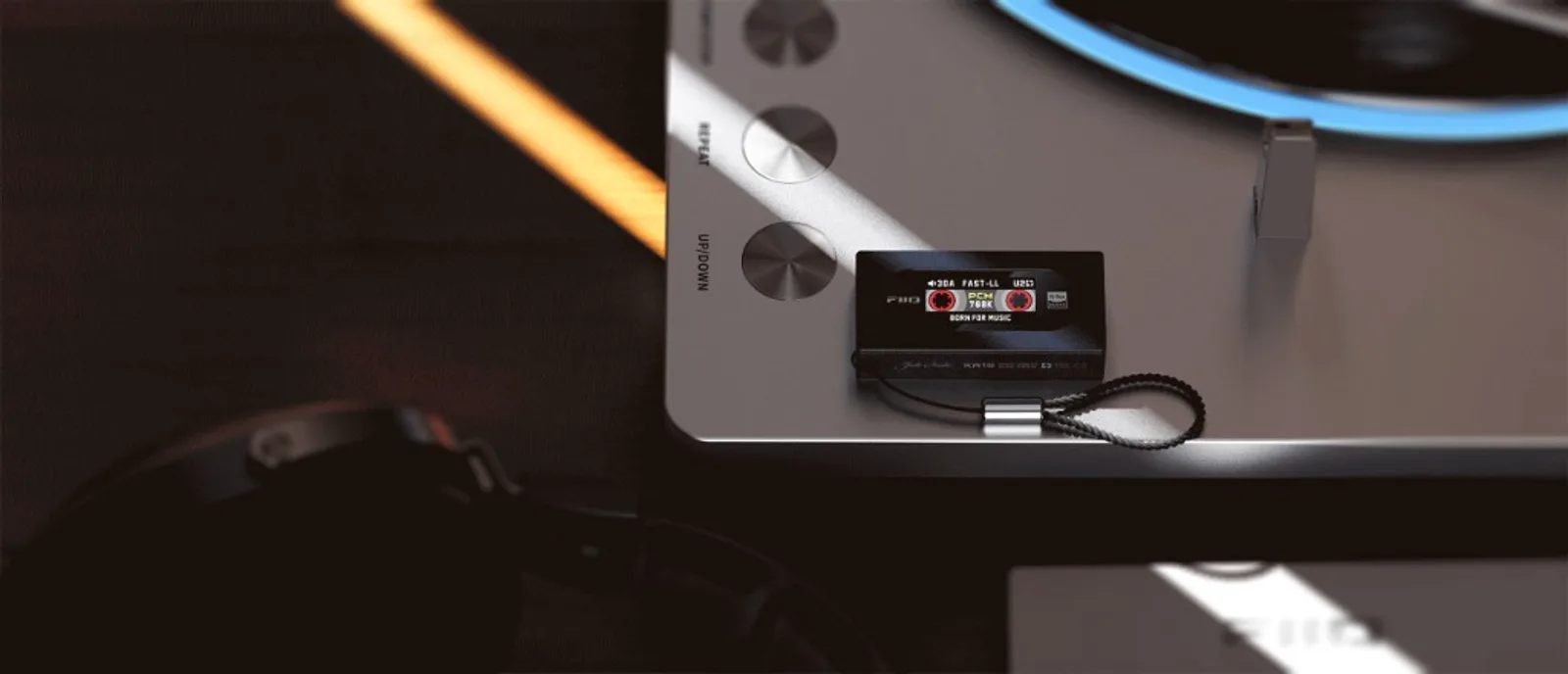 FiiO KA15 màu đen với màn hình cassette PCM 768K, đặt trên mặt kim loại cùng nút điều khiển và dây đeo