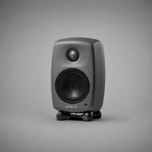 Genelec 8010A đen mờ mặt trước nền xám trung tính: tweeter và woofer lưới, logo GENELEC trắng, LED xanh lá, Iso-Pod đen, ánh sáng studio mềm