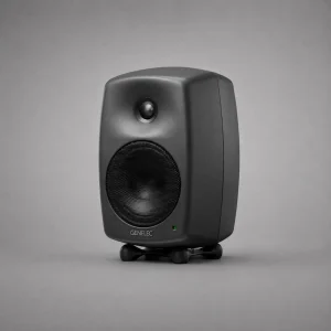 Genelec 8030C màu xám đậm Producer Finish góc ba phần tư trên nền xám studio: MDE, tweeter và woofer lưới đen, logo GENELEC sáng, LED xanh lá, Iso-Pod đen, ánh sáng mềm