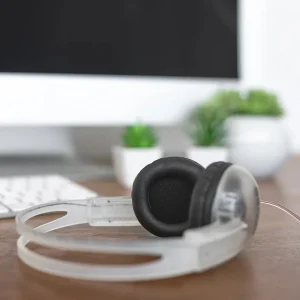 Tai nghe Koss CL-5i trong suốt đặt cạnh bàn phím và cây xanh, thiết kế on-ear gọn nhẹ