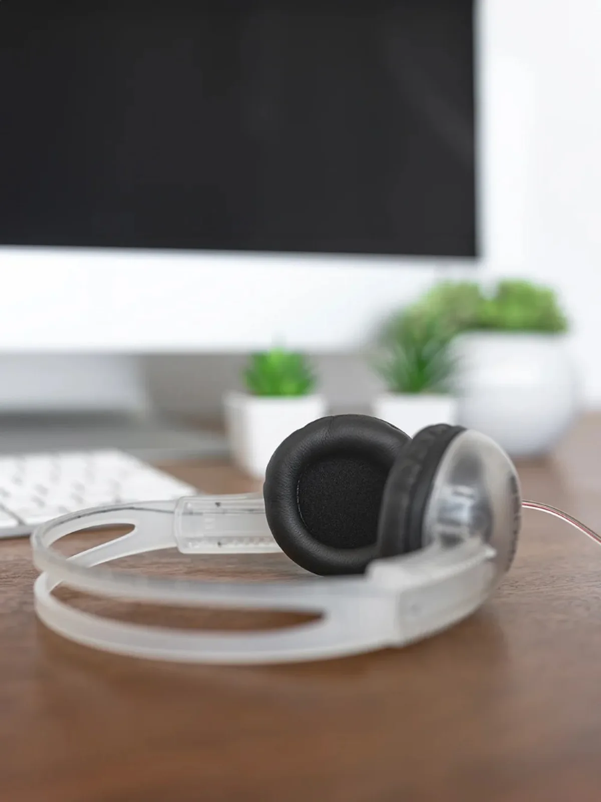 Tai nghe Koss CL-5i trong suốt đặt cạnh bàn phím và cây xanh, thiết kế on-ear gọn nhẹ