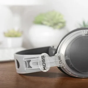 Tai nghe Koss CL/80 trong suốt đặt trên bàn gỗ, logo KOSS và model CL/80 trên khung headband