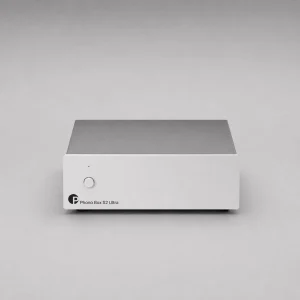Pro-Ject Phono Box S2 Ultra: phono preamp vỏ nhôm bạc lớn, mặt trước tối giản với nút tròn, đèn báo nhỏ và chữ Phono Box S2 Ultra, nền xám studio