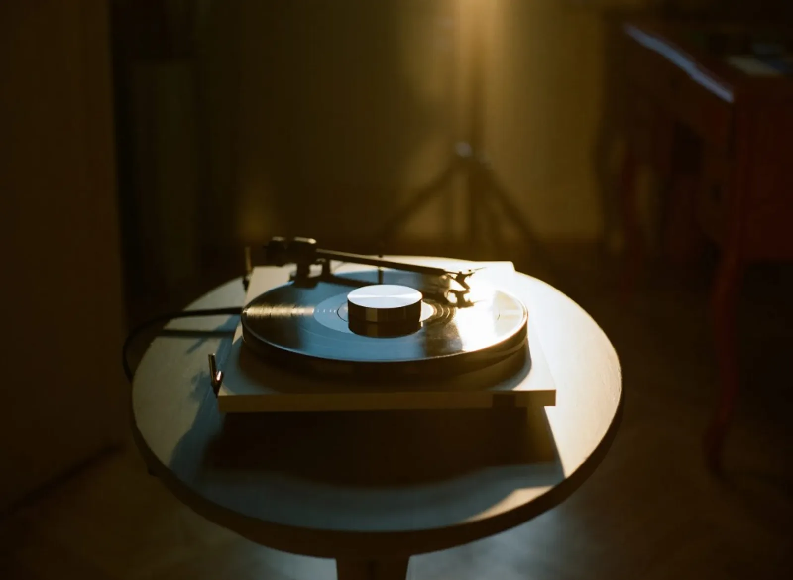 Pro-Ject Record Puck E bạc trên đĩa than, máy quay trắng và ánh sáng vàng ấm