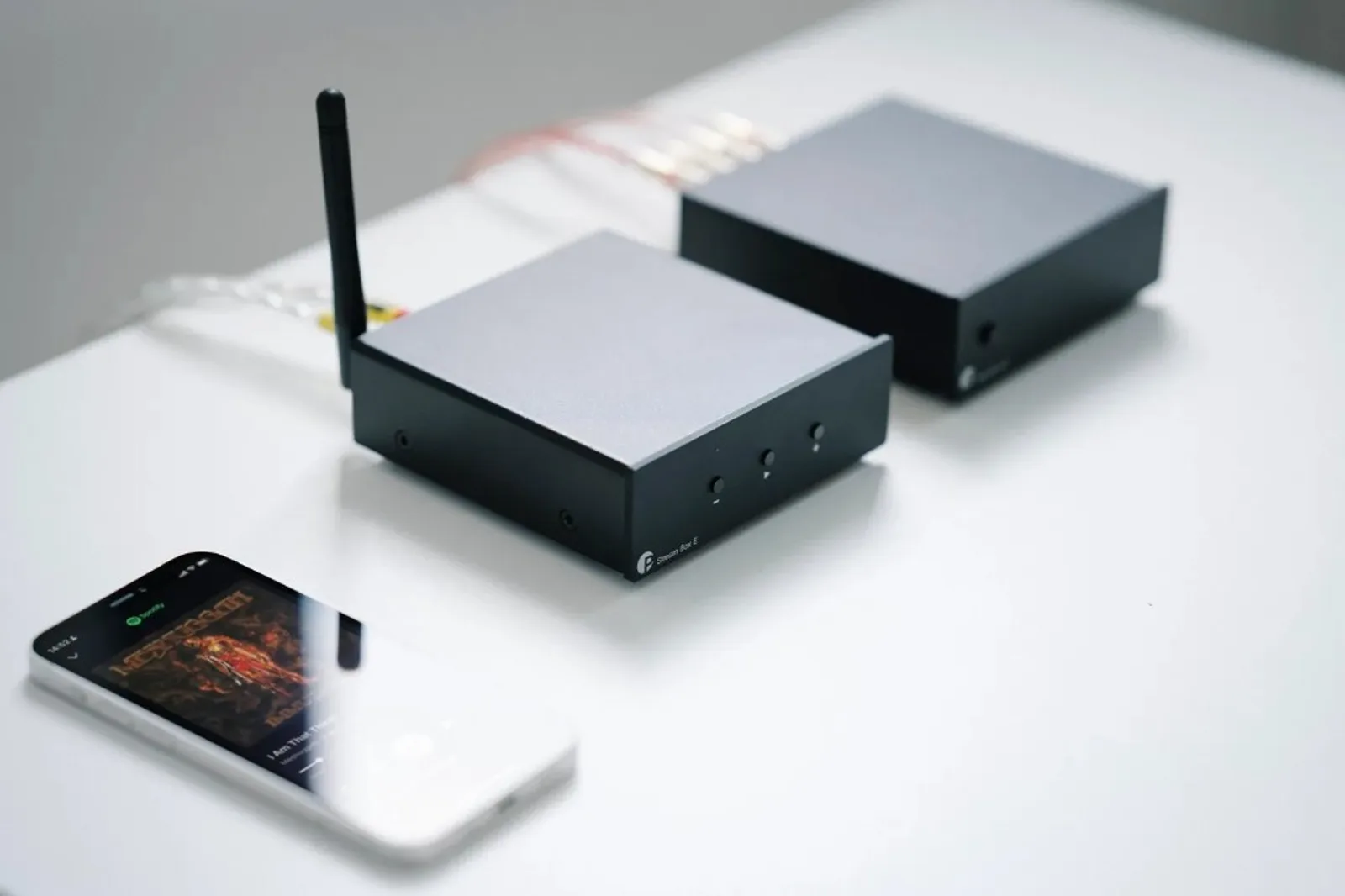Kệ hi-fi: Pro-Ject Stream Box E (mặt bạc) và Amp Box S3 cùng tông màu, loa bookshelf, đèn và kệ sách — không gian phòng khách ấm