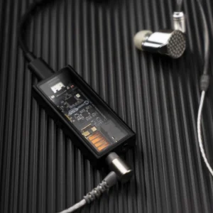 Questyle M15i mặt trong suốt lộ chip ESS và tụ cam, nối USB-C và tai nghe in-ear kim loại dây bạc trên nền đen có vân dọc.
