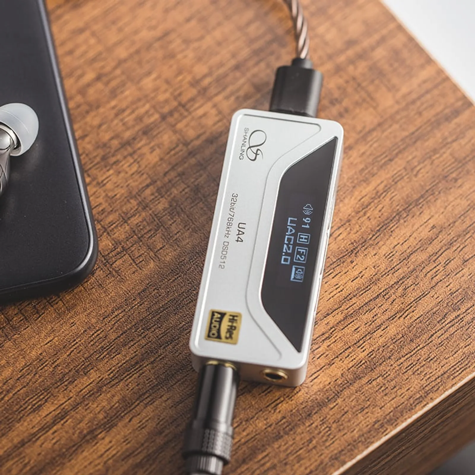 Shanling UA4 bạc trên bàn gỗ: USB-C nối smartphone, jack 4,4 mm cân bằng nối tai nghe; màn hiển thị UAC2.0, gain H, volume 91.