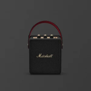 Loa Bluetooth Marshall Stockwell III màu đen với logo đồng, lưới loa và dây đeo lót đỏ trên nền xám