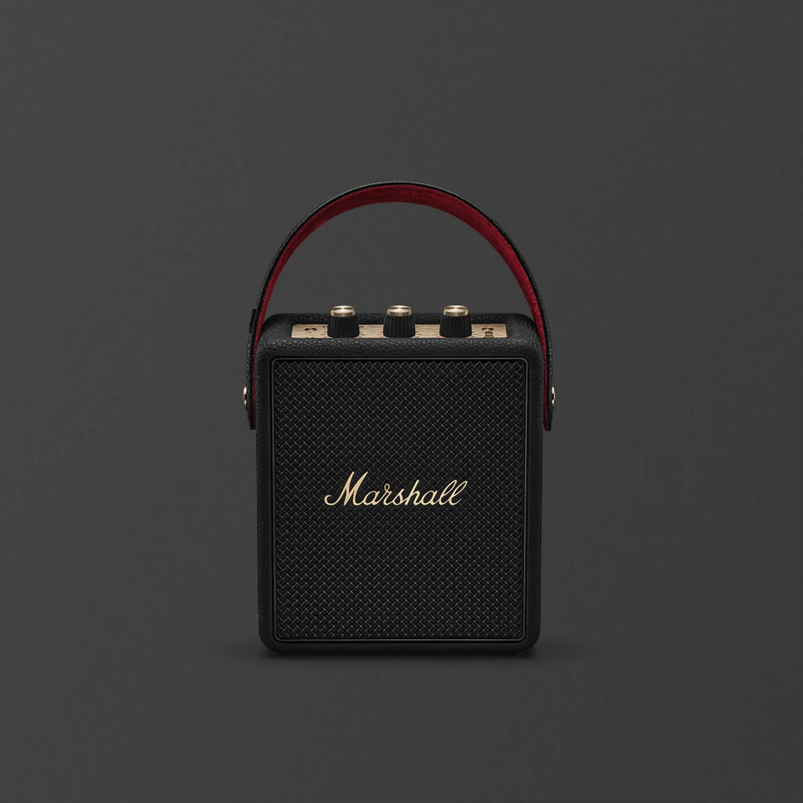 Loa Bluetooth Marshall Stockwell III màu đen với logo đồng, lưới loa và dây đeo lót đỏ trên nền xám