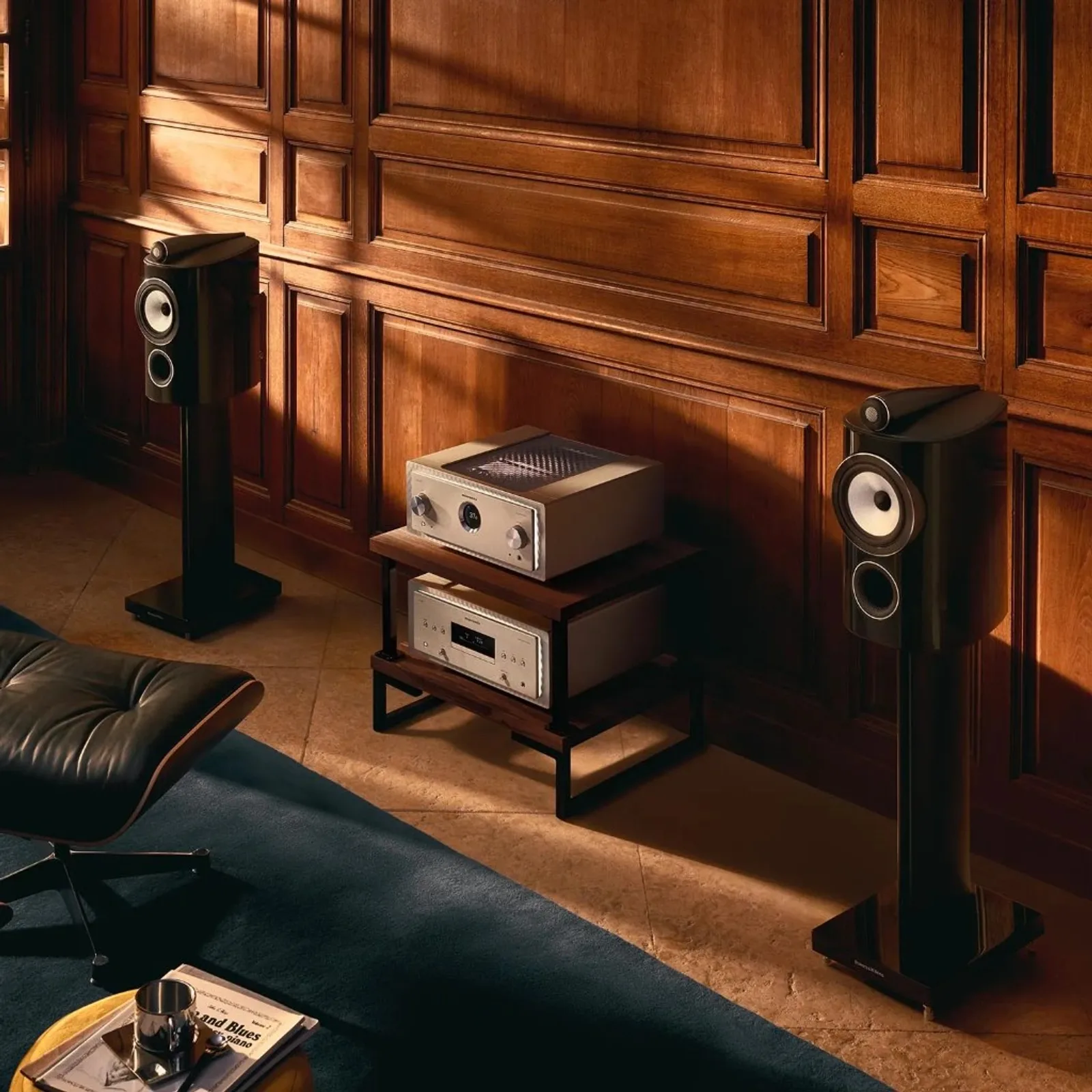 Đôi loa Bowers & Wilkins 805 D5 đen bóng trên chân đứng, phòng nghe gỗ tối với ánh sáng xuyên