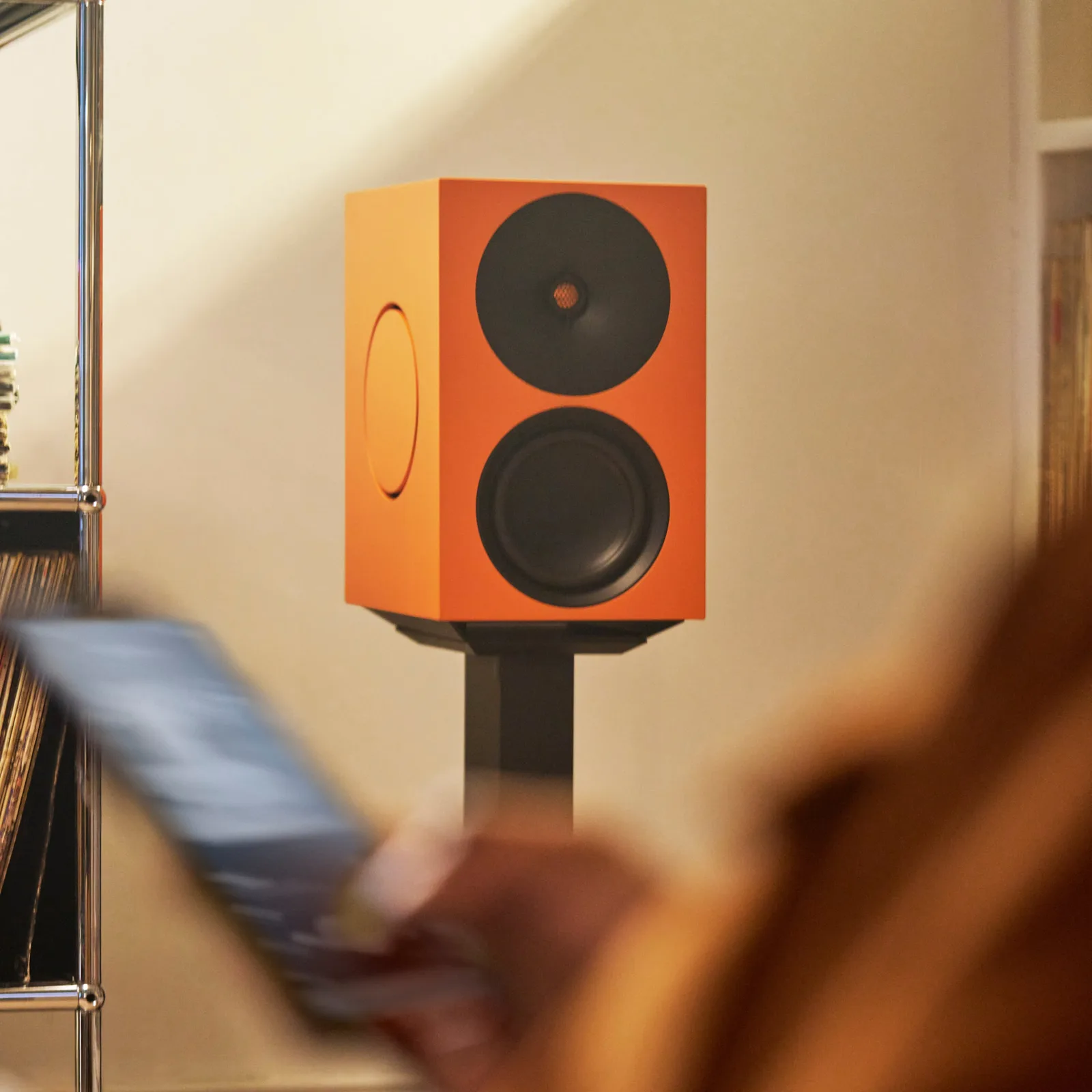 Cambridge Audio L/R X cam trên chân trong phòng ấm, người dùng smartphone phía trước