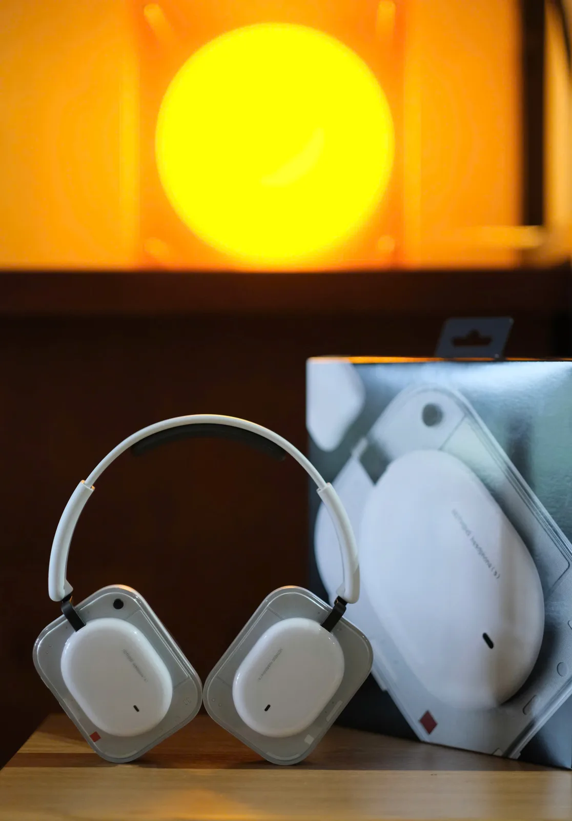 Nothing Headphone (a) màu trắng đứng cạnh hộp retail tại District M, nền ánh sáng vàng bokeh