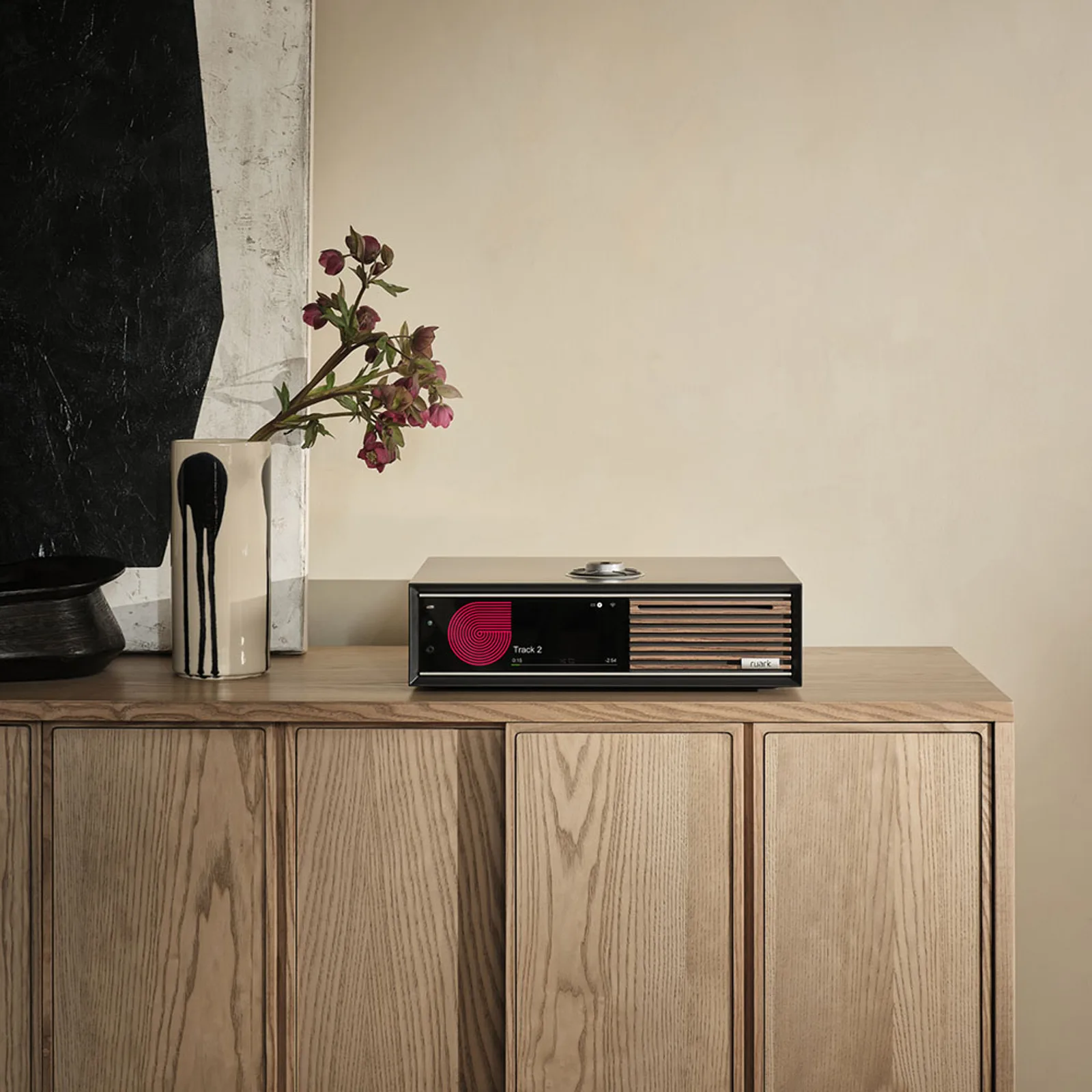 Ruark R710 Satin Charcoal trên tủ gỗ sáng cạnh tranh đen trắng