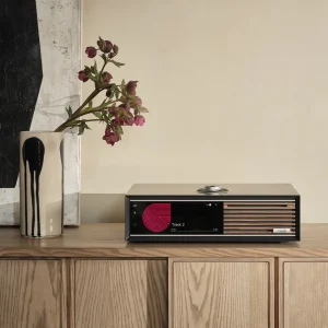 Ruark R710 Satin Charcoal trên sideboard gỗ, bình hoa và tranh trừu tượng