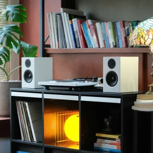 Mâm AT-LP70XBT và loa A28W trắng đặt giữa kệ gỗ, cây monstera và đèn Tiffany